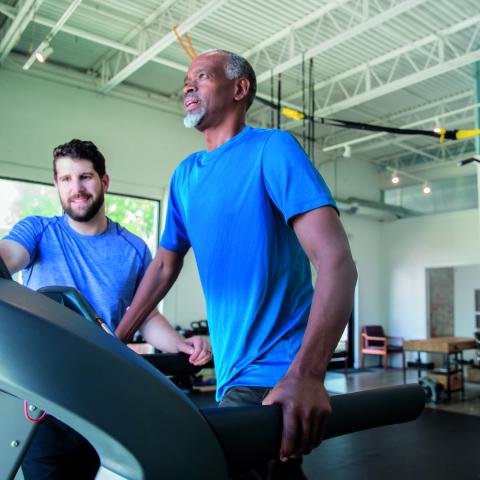Physical therapist assists participant on treadmill during spinal stimulation and gait training study at Kessler Foundation.