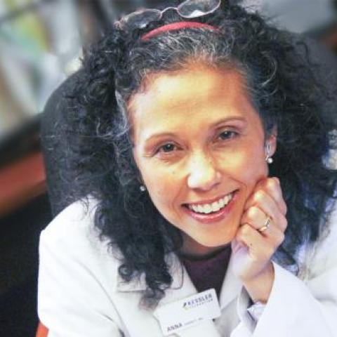 A.M. Barrett, PhD posing with left hand on her cheek wearing a labcoat
