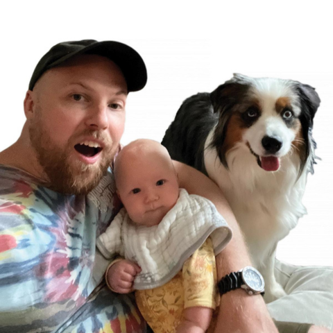 A man is holding a baby with a dog beside them. A man is holding a baby with a dog beside them.