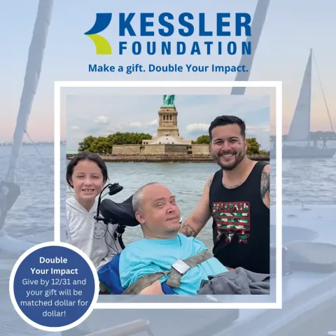 A man using a power wheelchair smiles for a photo with a young girl and a man. The statue of liberty is in the background.