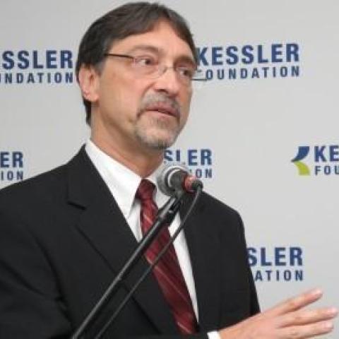 Dr DeLuca in front of kessler foundation logo