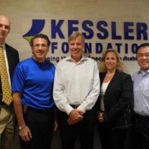 a group of people smiling in front of the kessler foundation banner