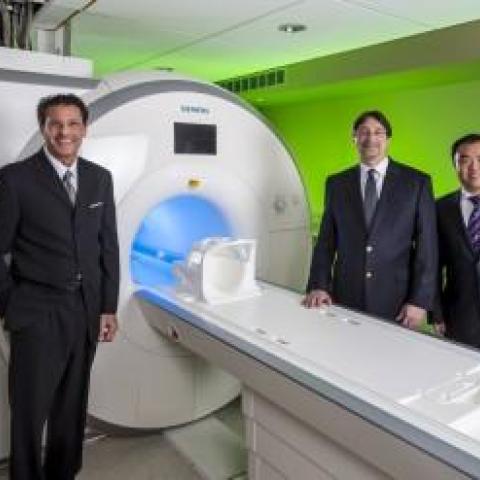 Rodger DeRose and 3 scientists stand in front of the MRI Machine