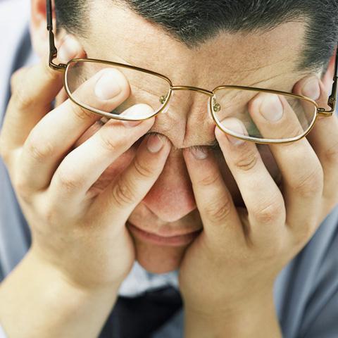 Man with eyeglasses having his down while rubbing his forehead