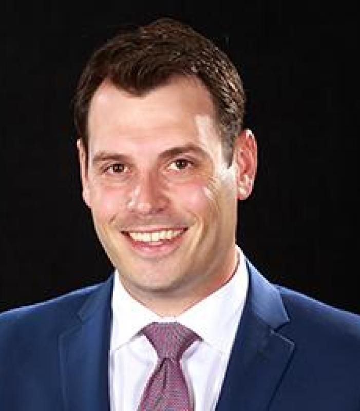 Director with navy blue suit and white collared shirt with tie smiling for the camera