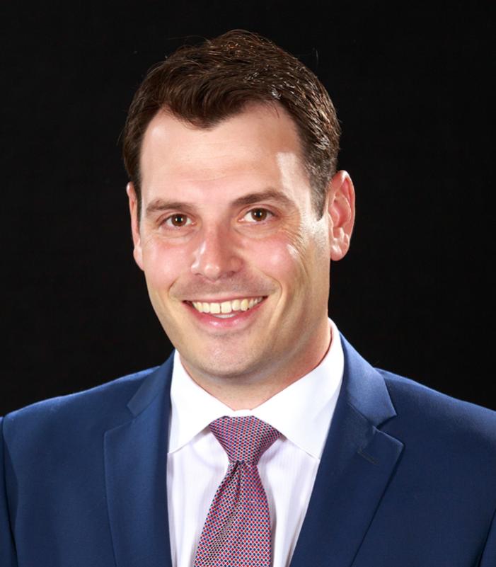 Director with navy blue suit and white collared shirt with tie smiling for the camera
