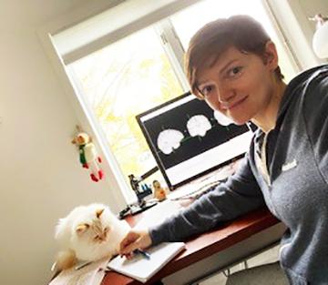 Dr. Ekaterina Dobryakova sitting next to her cat at her desk at home