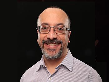 Director wearing collared shirt and glasses smiling for the camera