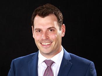 Director with navy blue suit and white collared shirt with tie smiling for the camera